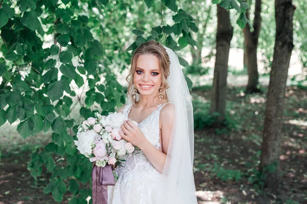 Hermosa novia joven celebración de ramo de boda y sonriendo a la cámara al aire libre — Foto de Stock