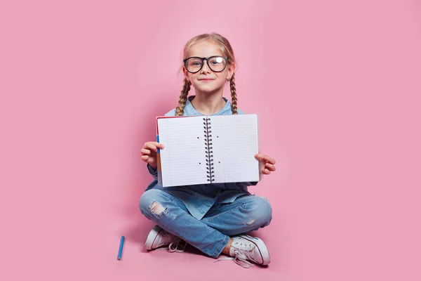 분홍색 배경에 시험지를 보여 주는 안경을 쓴 행복 한 어린 소녀 — 스톡 사진