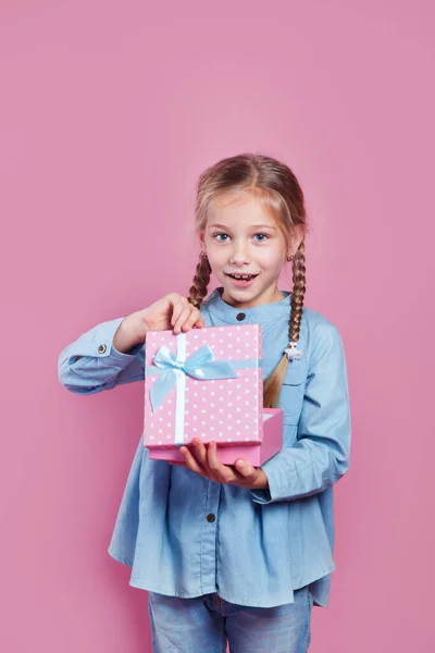Χαρούμενο κοριτσάκι που κρατάει ροζ δώρο στα χέρια του στο ροζ backgorund — Φωτογραφία Αρχείου