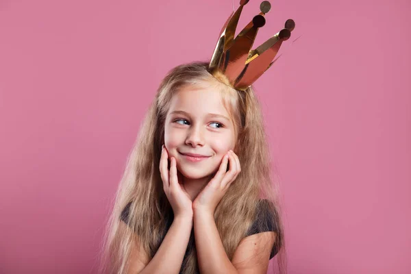 Портрет милой улыбчивой маленькой девочки в платье принцессы и корона на розовом фоне — стоковое фото