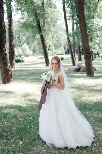 Impresionante novia joven en vestido blanco que sostiene ramo en el parque — Foto de Stock