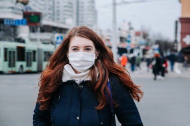 Balkon montlu genç Avrupalı kadın, şehirde tek kullanımlık koruyucu tıbbi maske.