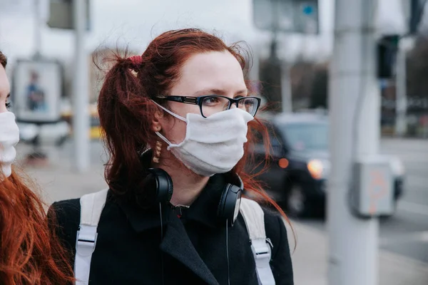 Ung europeisk kvinna i kal rock, skyddande engångs medicinsk mask på stadens gata — Stockfoto