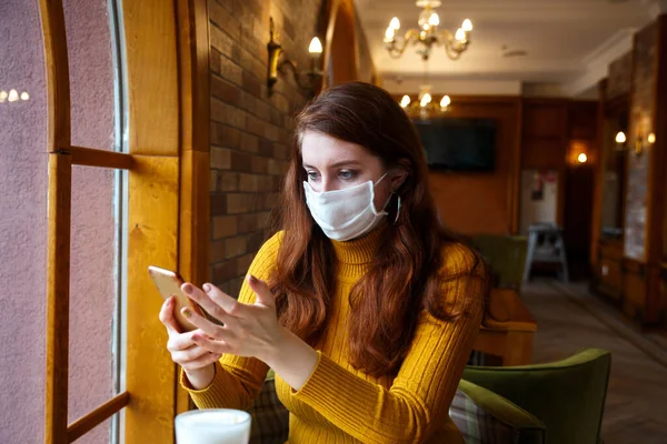 Donna seria con maschera protettiva guardando le notizie di controllo dello smart phone nel caffè — Foto Stock