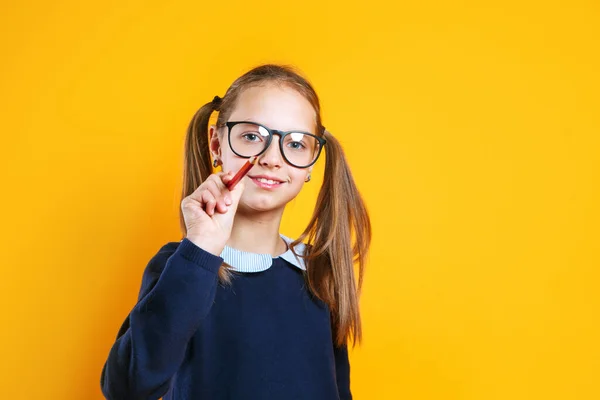 Školačka v brýlích ukazuje tužkou na prázdné místo pro text. — Stock fotografie