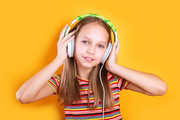 teenager girl in green headphones listens to music and sings song on a yellow background