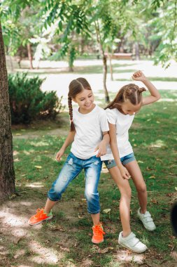 Beyaz tişörtlü iki küçük kız parkta eğleniyor..