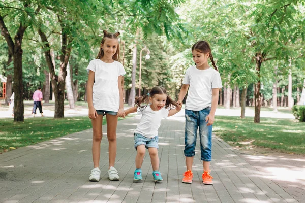 Tres niños con camisetas blancas están de pie tomados de la mano en el parque. Prepárate. . — Foto de Stock