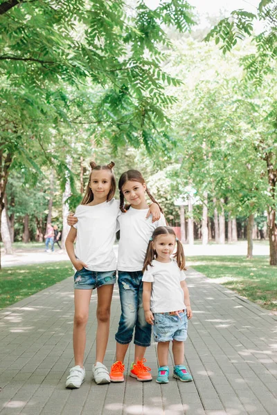 Tres niñas con camisetas blancas de pie y abrazadas en el parque. Prepárate. . — Foto de Stock
