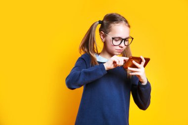 Şirin küçük kız sarı arka planda akıllı telefonuyla oynuyor. Modern çocuklardaki cihazlara bağımlılık.