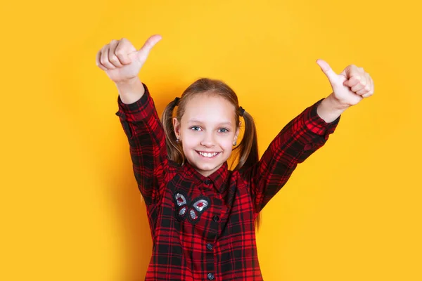 Portrét šťastné dívky ukazující palce nahoru gesto na žlutém pozadí — Stock fotografie