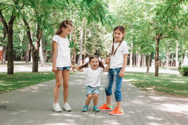 Beyaz tişörtlü üç çocuk parkta el ele tutuşuyorlar. Model.