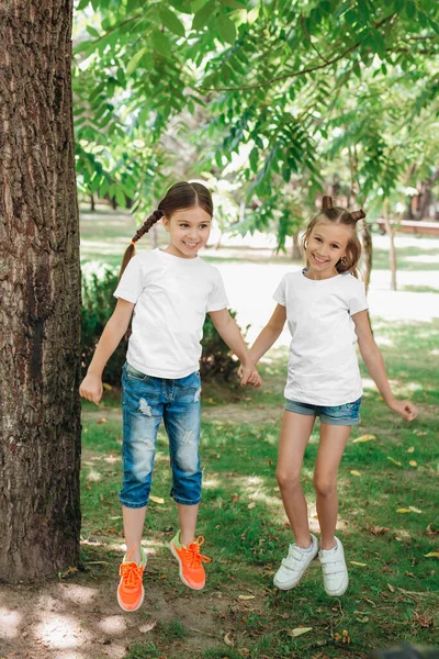 Två små flickor i vita t-shirts hoppar i parken utomhus. — Stockfoto