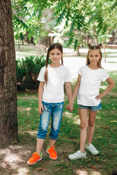 Dos niñas con camisetas blancas están de pie tomadas de la mano en el parque al aire libre. Prepárate. . — Foto de Stock