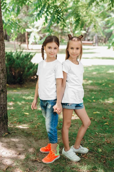 Dos niñas con camisetas blancas están de pie tomadas de la mano en el parque al aire libre. Prepárate. . — Foto de Stock