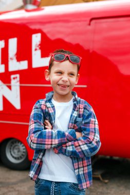 Kırmızı arka planda kareli gömlek ve güneş gözlüğü takan komik küçük çocuk.