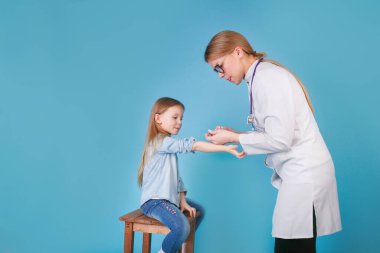 Genç bir kadın çocuk doktoru küçük bir kızın aşısını gerçekleştiriyor..