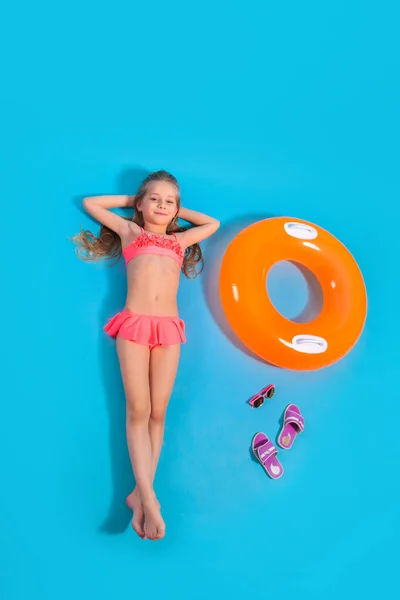Mavi stüdyo arka planında şişirilebilir bir daire ve terliklerle yerde yatan küçük bir kızın en iyi görüntüsü.