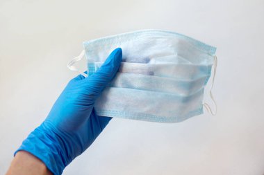 Beyaz arka plandaki enfeksiyondan korunmak için doktorun elinin tıbbi yüz maskesi ile yakın plan görüntüsü.