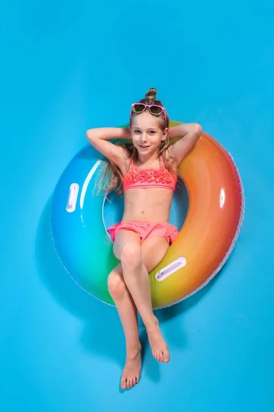 Mayo giymiş küçük bir kız sarı stüdyo arka planında şişirilebilir bir renk yüzüğünün üzerinde yatıyor..