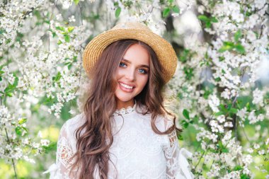 Hasır şapkalı genç bir kadın kameraya bakıyor. Bahar çiçekleri.