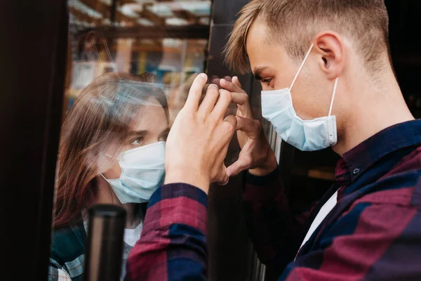 Young woman in a respiratory mask communicates with her boyfriend through a window. Coronavirus covid-19. Couple separated by Corona Covid-19 virus