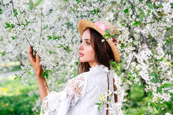 Bahar çiçekleri bahçesinde hasır şapkalı romantik genç bir kadın.