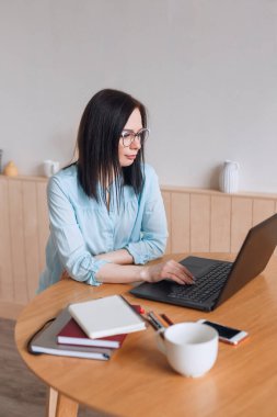 Gözlüklü, bilgisayarlı ve akıllı telefonlu bir kadın, ev ofisinde çalışıyor..