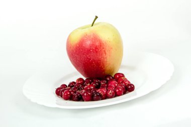 Beyaz arka planda kızılcıklı beyaz bir tabakta büyük kırmızı bir elma.