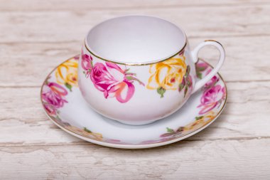 Boş beyaz bir porselen bardak. Hassas pembe ve sarı gül tomurcukları ahşap bir zeminde..