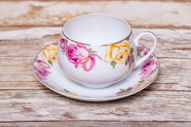 Boş beyaz bir porselen bardak. Hassas pembe ve sarı gül tomurcukları ahşap bir zeminde..