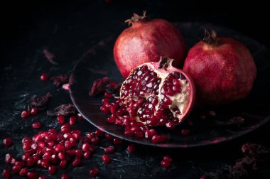 Karanlık bir taş zemin üzerinde hayat dolu nar ağaçları.