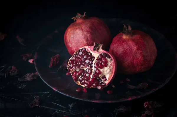 Karanlık bir taş zemin üzerinde hayat dolu nar ağaçları.