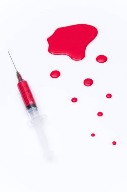 Beyaz bir zemin üzerinde kırmızı kan lekesi olan tıbbi şırınga.
