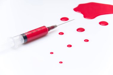 Beyaz bir zemin üzerinde kırmızı kan lekesi olan tıbbi şırınga.