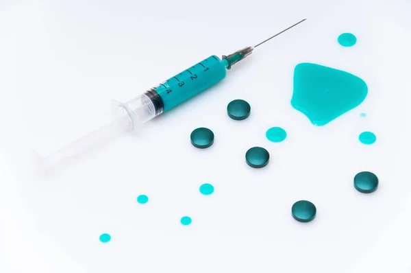 Yeşil haplarla çevrili beyaz bir zemin üzerinde yeşil sıvı bulunan tıbbi şırınga