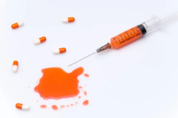 Turuncu solüsyonlu bir şırınga beyaz bir arka planda yatıyor.