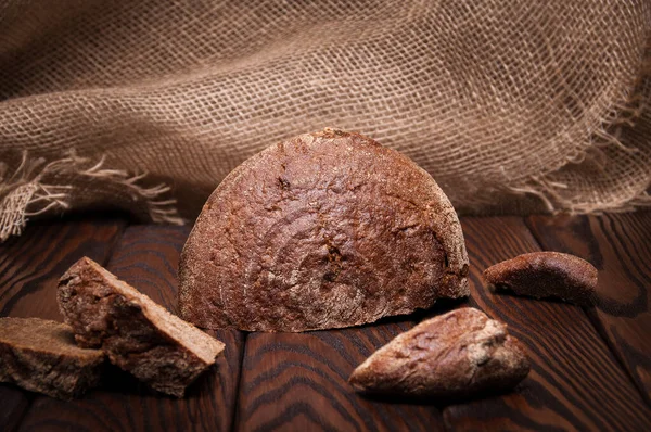 Kahverengi ahşap bir mutfak masasında bez bir çuval bezi üzerinde siyah ekmek hayatı