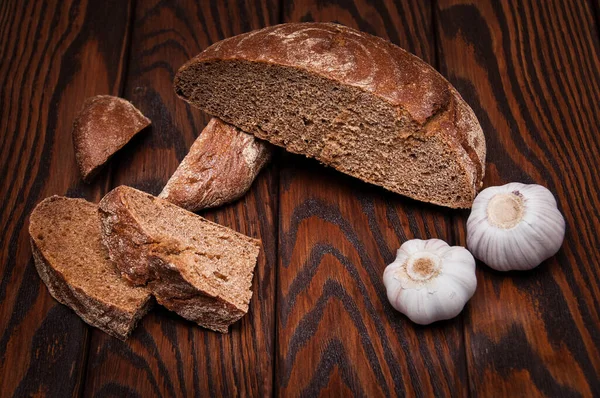 Kahverengi ahşap mutfak masasında bez çuval bezi üzerinde siyah ekmek ve sarımsak dolu bir hayat.