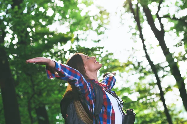 Young female hiker with binoculars and backpack in forest.