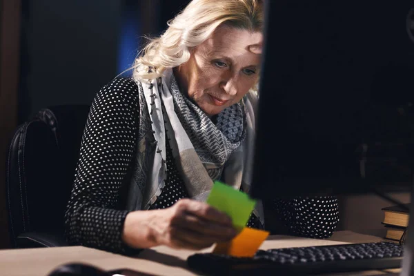 Blonde elderly woman working with computer on dark room background