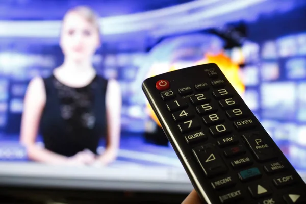 Close up Hand holding TV remote control with a television in the background. — Stock Photo, Image