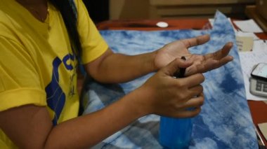 Taylandlı kadın kumaş maskesi dikiyor ve alkol jeli kullanıyor. El ve ürünleri temizliyor. Nonthaburi, Tayland 'daki atölyede çalışmaya başlamadan önce.