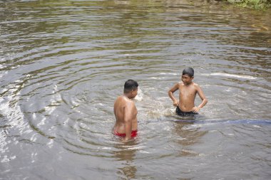 NARATHIWAT, THAILAND - 16 Ağustos 2019 'da Taylandlı çocuklar Narathiwat, Tayland' da Wadi Al Hussein veya Talo Mano Camii yakınlarındaki Bacho Tak Bai köyündeki su birikintisinde oynayıp yüzüyorlar.