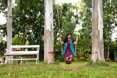 Taylandlı kadın rahatlayıp, Thailand 'ın Ratchaburi Eyaleti' ndeki Ban Pong 'daki Mae Khlong ya da Meklong nehrinin kıyısındaki tatil köyünün bahçesindeki ahşap salıncaklarda oynuyor.