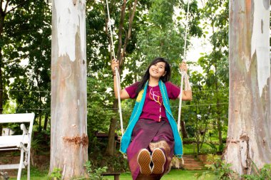 Taylandlı kadın rahatlayıp, Thailand 'ın Ratchaburi Eyaleti' ndeki Ban Pong 'daki Mae Khlong ya da Meklong nehrinin kıyısındaki tatil köyünün bahçesindeki ahşap salıncaklarda oynuyor.