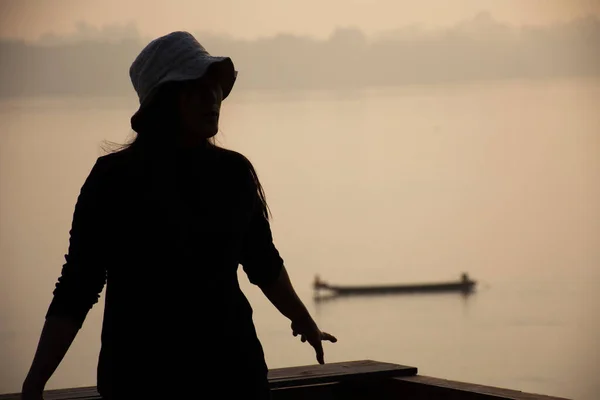 タイのムクダハンで朝の時間にメコン川のロングテールボートと反射光水面と太陽の照明を持つシルエットタイの女性 — ストック写真