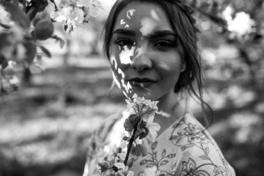 Güzel, genç, esmer bir kadın elma ağacının yanında duruyor.