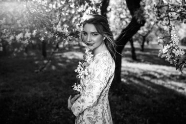 Güzel, genç, esmer bir kadın elma ağacının yanında duruyor.