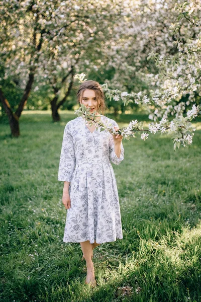 Beautiful young brunette woman standing near the apple tree on a — Stock Photo, Image